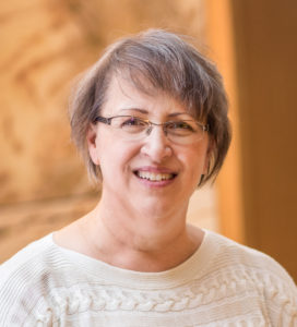 headshot of Cindy Kolbe, middle aged woman, short grey and brown hair, glasses, smiling 