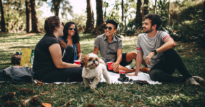 College students having a picnic, smiling. small dog also in the picture