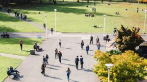 Birds eye picture of a college quad. Green grass and paved paths with students walking around.