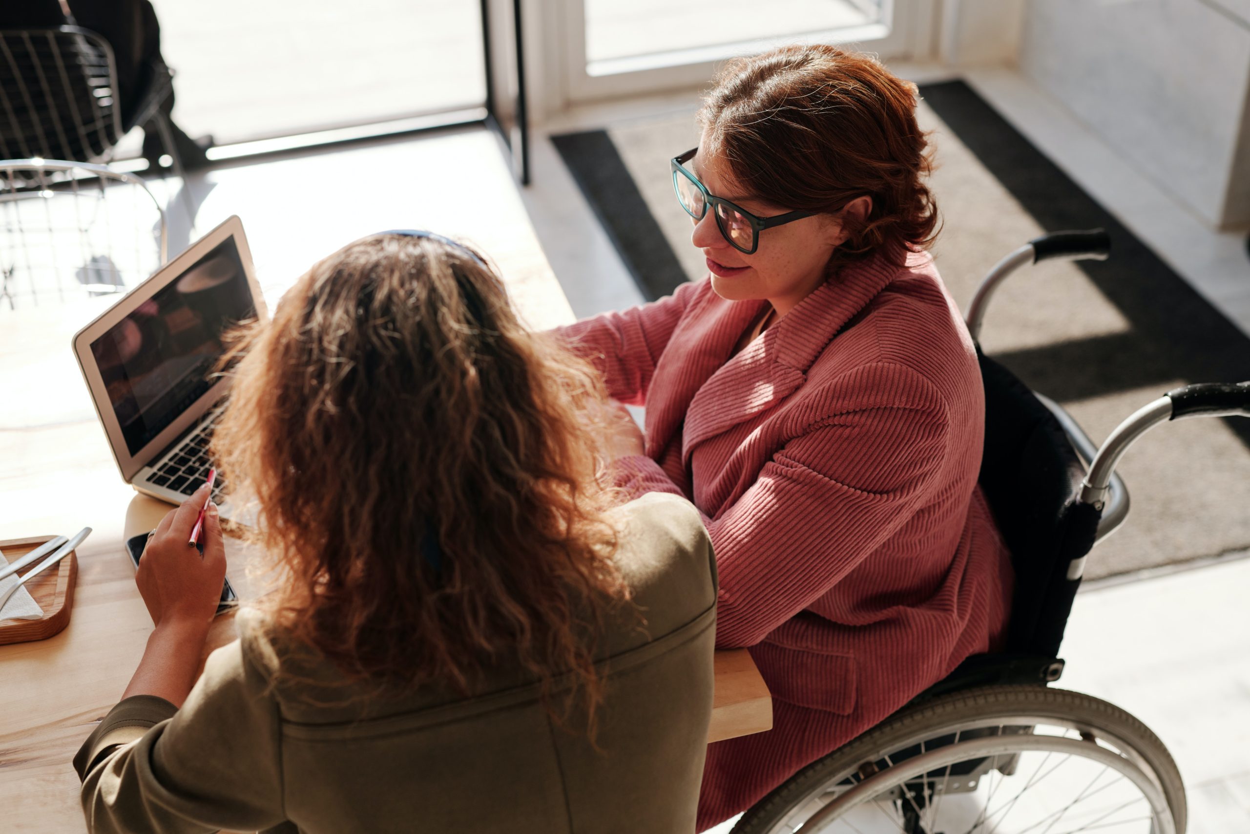 two women one in a wheel chair sitting down on a table