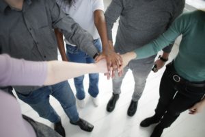 hands of people with different skin tones clasped on top of each other.