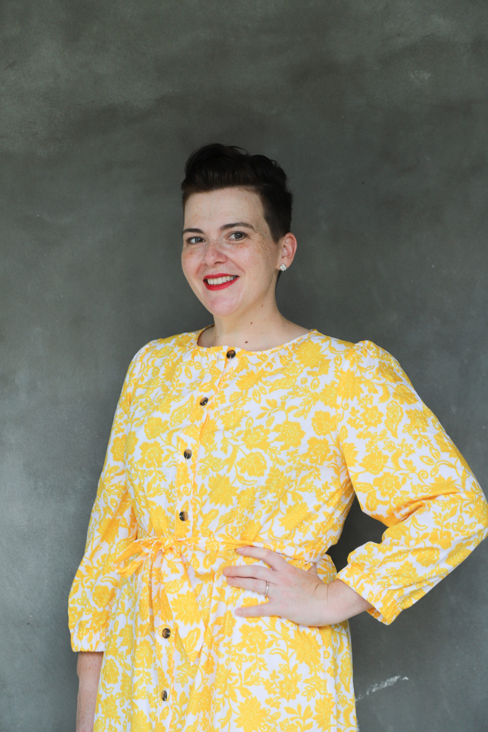 Annie Tulkin, wearing a yellow dress, hand on hip , smiling