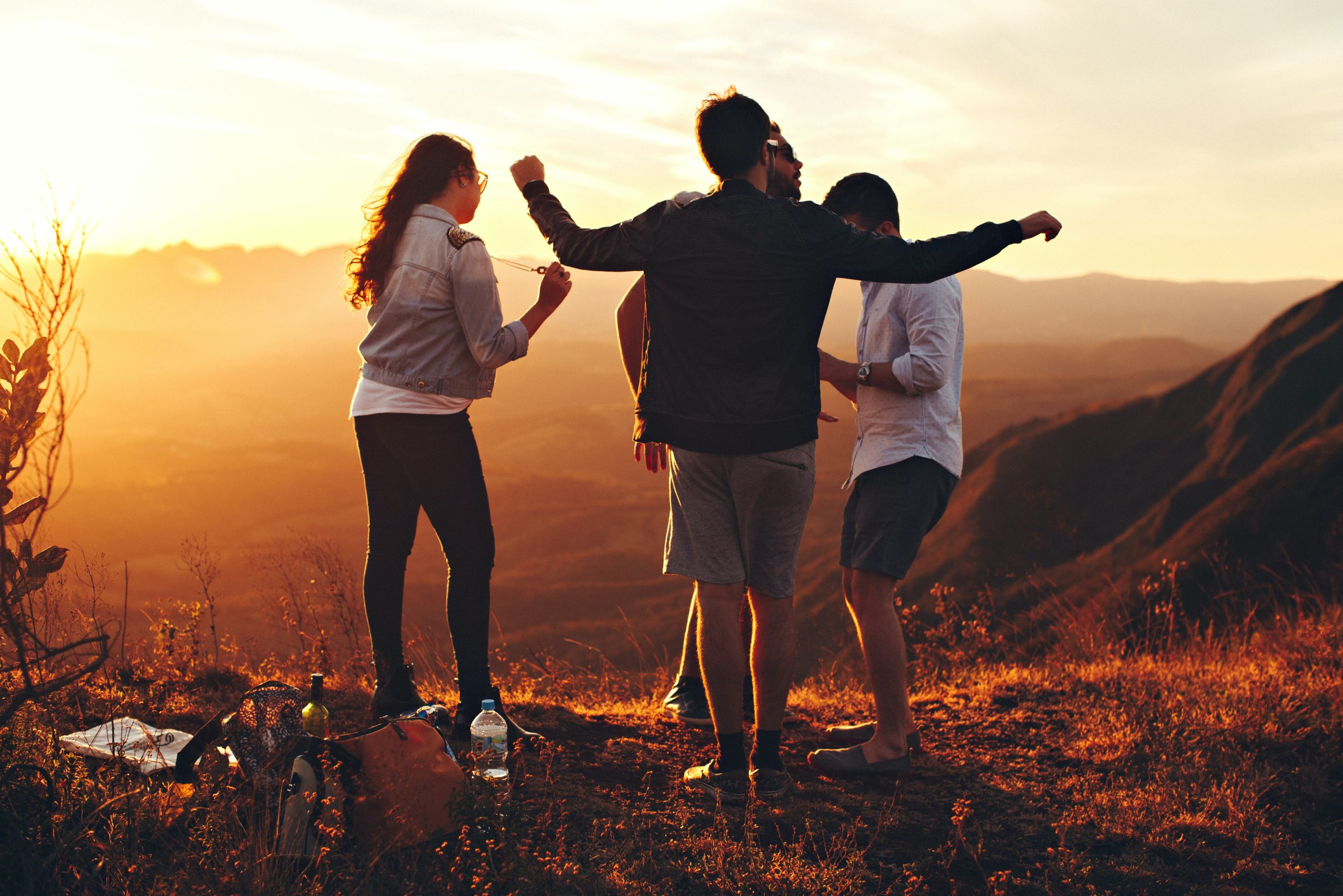4 young adults on a mountain with the sun setting. Dancing and joyful