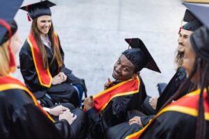 Colleges students in graduation attire. 2 students using wheelchairs and others standing around