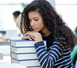 Young woman with light brown skin and long wavy hair, resting her head on a pile of books
