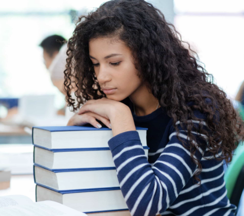 Young woman with light brown skin and long wavy hair, resting her head on a pile of books