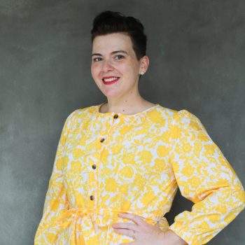 Annie Tulkin, wearing a yellow dress, hand on hip , smiling